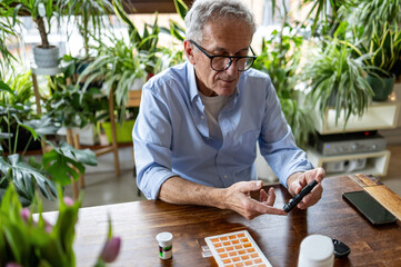 Mature man checking his blood sugar level while sitting at home
