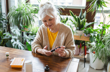 Elderly woman checking her blood sugar level while sitting at home
- 762350411