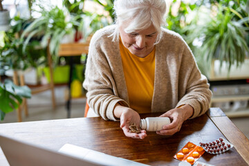 Senior woman taking pills from a bottle while sitting at the table at home
- 762350453