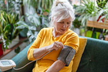 Senior woman measuring her blood pressure while sitting on a sofa at home
