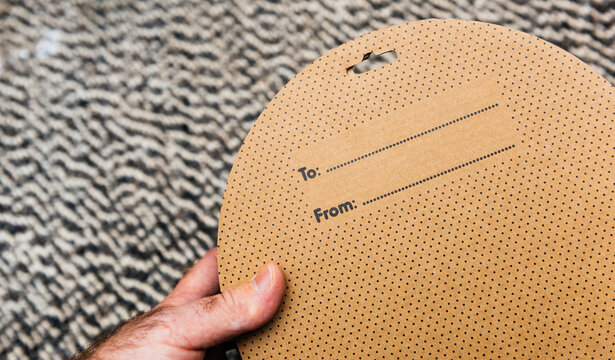 Male hand holds cardboard round box featuring To and From label with space to write names, perfect for gifting and personalizing packages