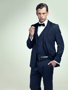 Portrait, serious or young gentleman smoke a cigarette in studio, confidence or vintage fashion by white background. Face, tobacco or man in retro suit or tuxedo, bowtie or hands in pocket for class
