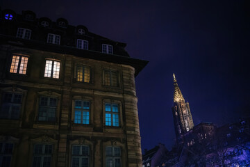 A stunning view of a luxury real estate building with an illuminated window, set against the backdrop of the iconic Notre-Dame Cathedral under a clear blue sky