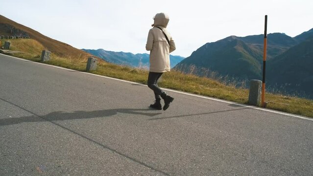Beautiful woman traveler walks along Majestic Grossglockner Mountain Road in Austria, snow covered sharp peaks of the alpine mountains on background. Incredibly beautiful views in the Alpine mountains