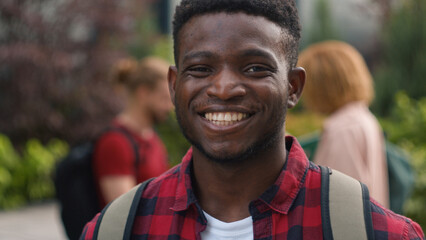 African American young student man guy smiling happy carefree pupil high school schoolboy smile at camera standing on background of talking diverse multiracial students friends education outdoors - obrazy, fototapety, plakaty