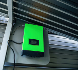 An industrial green solar power inverter installed on a metal garage wall, harnessing renewable...