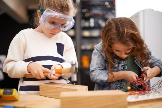 Children, construction and diy in workshop with tools, play and game in kitchen of home. Girls, hammer and safety glasses for wood project or building, carpentry and woodworking or manufacture