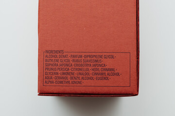 Ingredient list on a red perfume box detailing the chemical components used in the fragrance, set against a clear background - obrazy, fototapety, plakaty