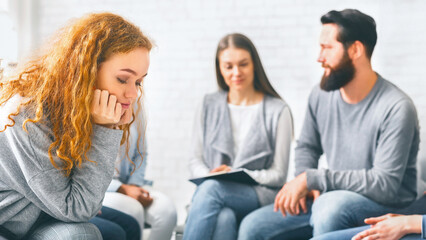 Upset redhead woman sitting at group therapy session