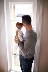 Fototapeta premium Father, baby and bonding with love and window, growth and child development with view at family home. Man, infant or newborn with back and dad holding kid for comfort, childhood and parenting