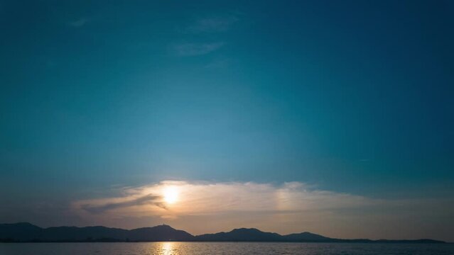 Time lapse Blue sky above the ocean at sunset. The sun's rays glimmered on the horizon.The sun floats above the mountain peaks in the evening. sparkling water reflection. bright blue sky background