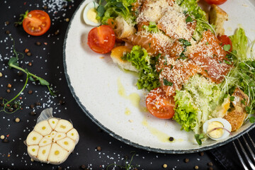 Classic Caesar salad with salmon. On a black stone background. In a plate, close-up.