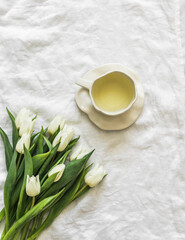 Obraz na płótnie Canvas A cup of green tea and a bouquet of white tulips on the white sheets of the bed