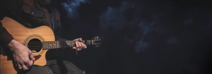 A man plays an acoustic guitar on a dark background with space for text.