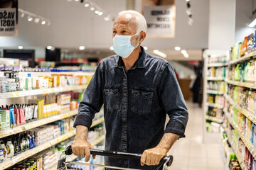 Man grocery shopping at the supermarket wearing a facemask. Caucasian man grocery shopping at the...