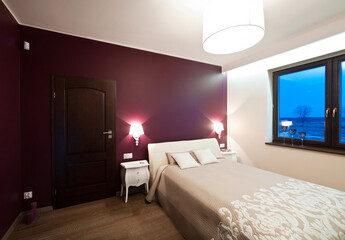 Elegant modern cozy bedroom with deep red headboard wall wall and illuminating sideboard lamps