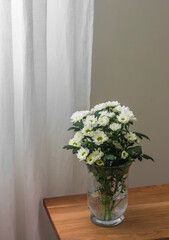 A bouquet of white chrysanthemums in a glass vase on a wooden bench in the living room