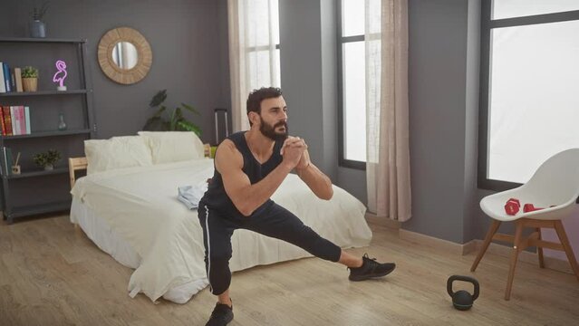 A bearded man exercises in a bedroom with weights and a neutral decor, illustrating an indoor fitness routine at home