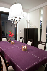 Nighttime view of an elegant dining room with purple tablecloth table in the center. Contemporary home European style design architecture