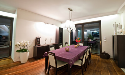Nighttime view of an elegant dining room with purple tablecloth table in the center. Contemporary...