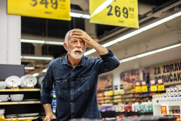 Mature man standing among the produce aisle at the supermarket and feeling upset about the increase...