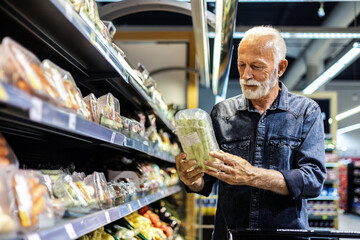 Smiling elderly man picking up vegetables in a grocery store.