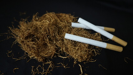 dry cut tobacco leaf, cigarettes and cigarette machine on black background. handmade cigarettes