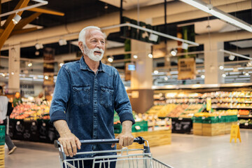 Cropped shot of mid 60's handsome man walking through supermarket aisle and buying some food during weekly grocery shopping. - obrazy, fototapety, plakaty