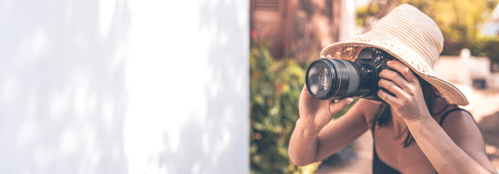 A woman in a hat takes pictures with a professional SLR camera on a summer day.