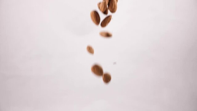 Close-up of almonds being spilled on a white background in slow motion. The nut falls from a height of about 6 inches and lands on the surface with a soft thud. frame rate of 240 frames per second