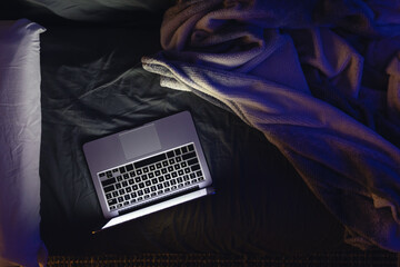Laptop with glowing screen on bed at night, top view, copy space. © puhimec