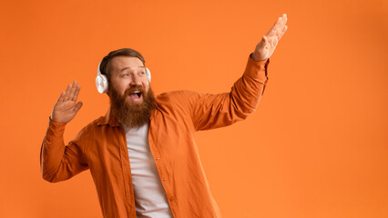 Positive Bearded Guy In Wireless Headset Dancing Over Orange Wall