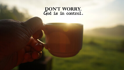 Morning inspirational quote - Don't worry. God is in control. With person holding a cup of coffee or tea against the warm sunrise light background. Faith and hope. Believe in God concept. - obrazy, fototapety, plakaty