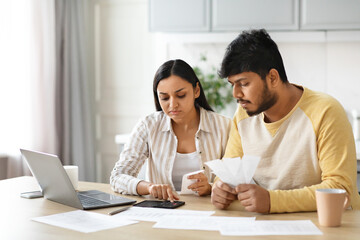 Unhappy millennial indian couple working on family budget