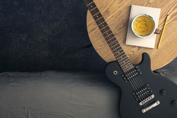 Musical background with electric guitar, notepad and cup of tea on the table.