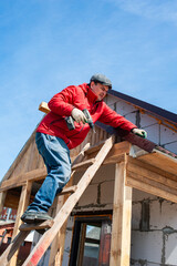A worker builds a roof in a house while standing on a wooden ladder. Blue sky