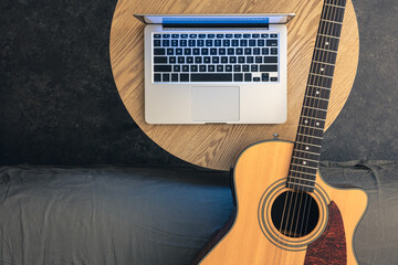 Acoustic guitar and laptop on a wooden table, top view.