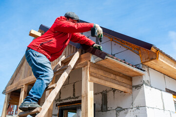 A worker builds a roof in a house while standing on a wooden ladder. Blue sky - 762393490