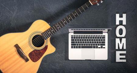Acoustic guitar, laptop and decorative word Home on a dark background, top view.