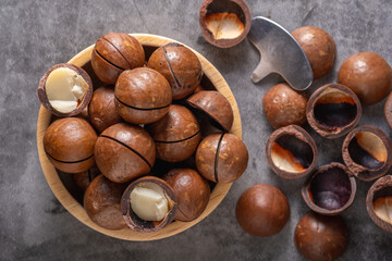 Macadamia nuts in wooden cup and  peeler on table, flat lay