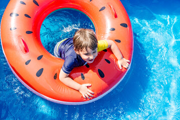 Beautiful cheerful boy swimming in the pool, having fun, laughing