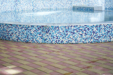 Side view of an outdoor swimming pool with blue and white mosaic ceramic tiles, with blue water. Background with copy space. Concept of summer, swimming, leisure time, vacation.