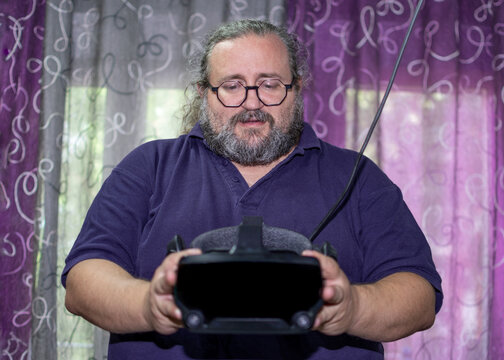 Overweight man with beard and glasses holding virtual reality on his hands