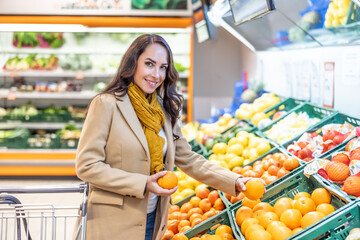 Woman shopping for groceries with a shopping cart. A young brunette buys fruit in a supermarket - 762403447