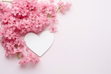 A white heart cutout framed by delicate pink cherry blossoms on a light wooden surface.