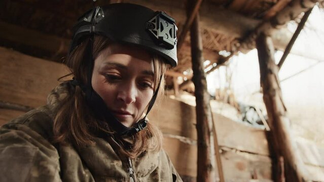 A focused woman soldier equipped with a helmet and tactical wear is inside a wooden bunker, preparing mentally for imminent action. Camera 8K RAW. 
