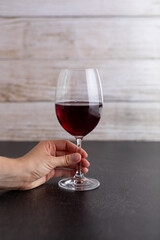 An isolated glass of red wine on a dark surface being held by a hand