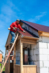 A worker builds a roof in a house while standing on a wooden ladder. Blue sky - 762407099