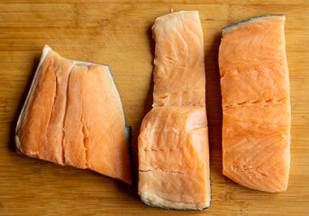  Close-up of raw, fresh salmon fillets arranged neatly on a wooden cutting board, showcasing their...