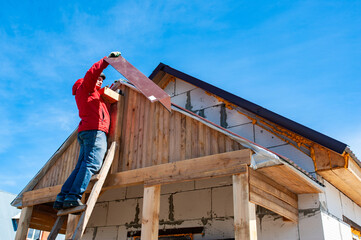 A worker builds a roof in a house while standing on a wooden ladder. Blue sky - 762407674
